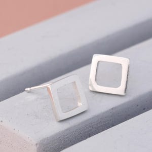 Polished silver stud earrings in square design on grey dish