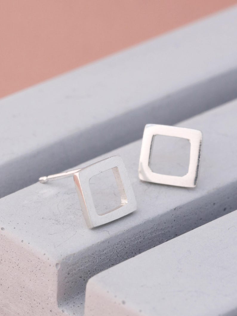 Polished silver stud earrings in square design on grey dish