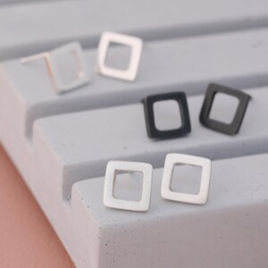Square stud earrings in silver and black finishes on grey dish, minimal earrings