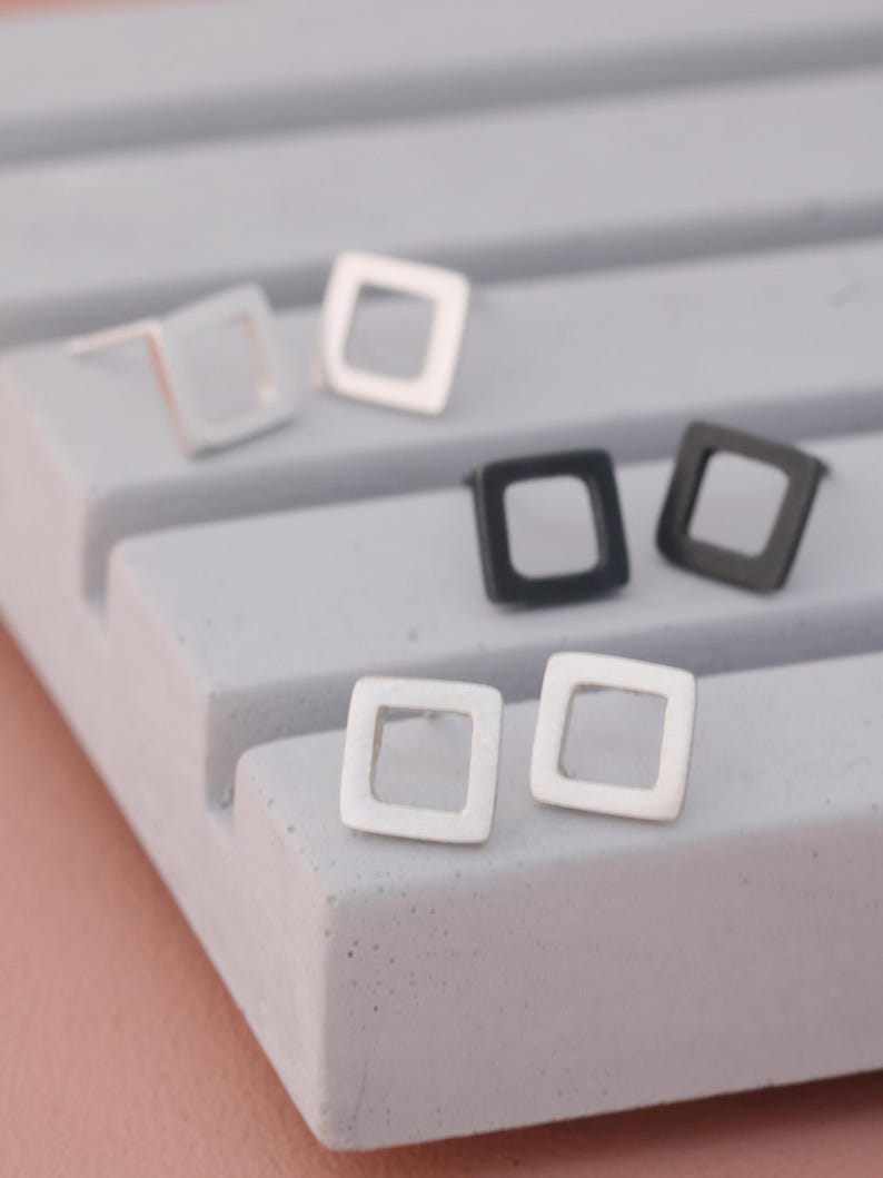 Square stud earrings in silver and black finishes on grey dish, minimal earrings