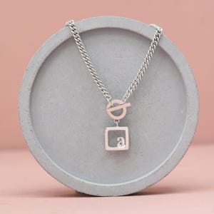 Collar con inicial en plata de ley. Collar con letra como regalo de cumpleaños. Collar con colgante con cierre de palanca. Collar con etiqueta con inicial.