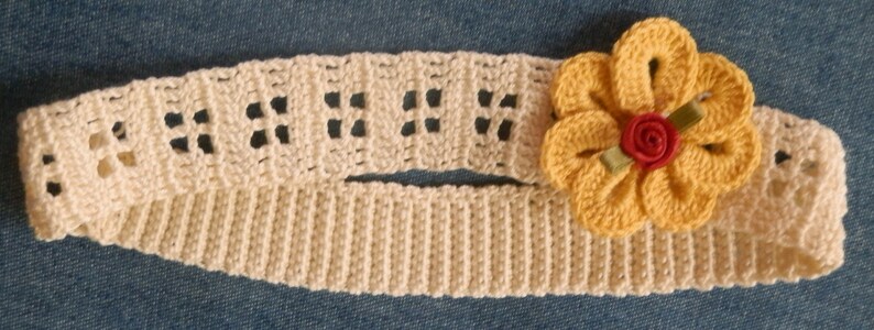 May include: A crocheted headband with a yellow flower accent. The headband is cream colored and the flower has a red center.