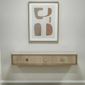 May include: A hallway with light wood flooring and light gray walls. A framed abstract art piece hangs above a wooden console table with three drawers and decorative knobs. The hallway leads to several doorways.