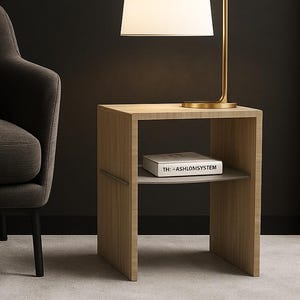 Può includere: Un tavolino moderno con una lampada dorata e un paralume bianco. Il tavolo è in legno chiaro e ha un ripiano con il libro "THE ASHLONSYSTEM". A sinistra c'è un divano grigio scuro con un cuscino.