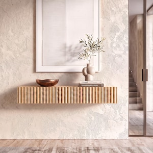 May include: A light wood floating console table with a vertical slatted front design. On top sits a copper-toned bowl, a beige ceramic vase with a leafy branch, and two stacked books with the visible text Donel and INNOCUOUS STYLE & DESIGN.