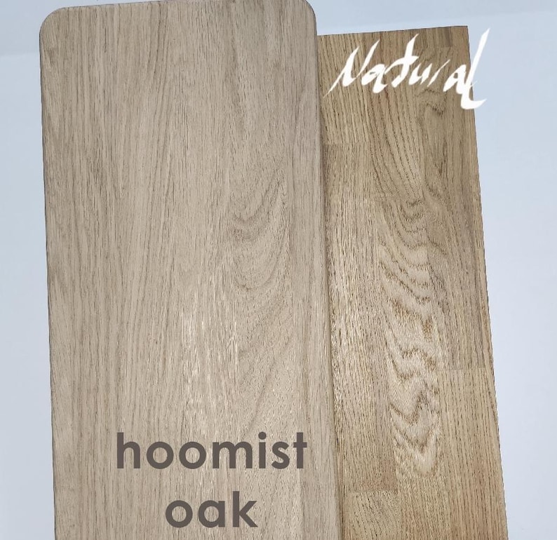 May include: Two rectangular wooden boards with visible grain patterns. The left board is labeled hoomist oak in dark text, and the right board is labeled Natural in white script. Both pieces display light brown wood tones with distinct textures.