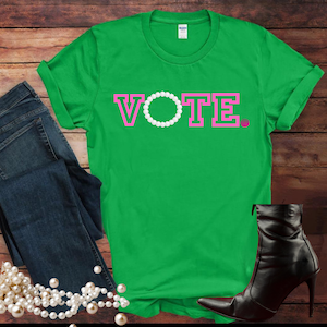 以下が含まれることがあります： ピンクの文字で「VOTE」と書かれた緑色のTシャツ。Oの文字は白い真珠のネックレスに置き換えられています。