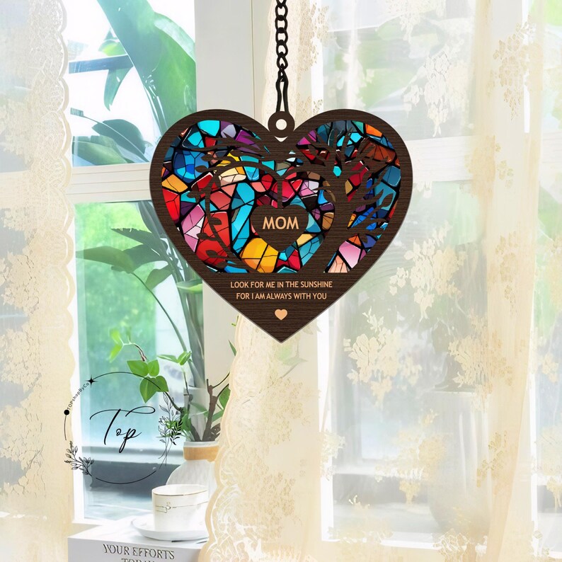 May include: A wooden heart-shaped wind chime with a stained glass design in shades of blue, red, yellow, and green. The chime features the word "MOM" and the text "Look for me in the sunshine for I am always with you".