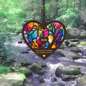 May include: A wooden heart-shaped wind chime with a stained glass design in shades of blue, green, yellow, orange, pink, and purple. The wind chime features a tree with a heart in the center that says "MOM" and the text "Look for me in the sunshine for I am always with you".