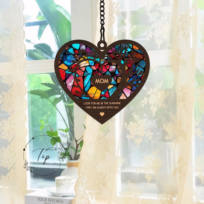 May include: A wooden heart-shaped wind chime with a stained glass design in shades of blue, red, yellow, and green. The chime features the word "MOM" and the text "Look for me in the sunshine for I am always with you".