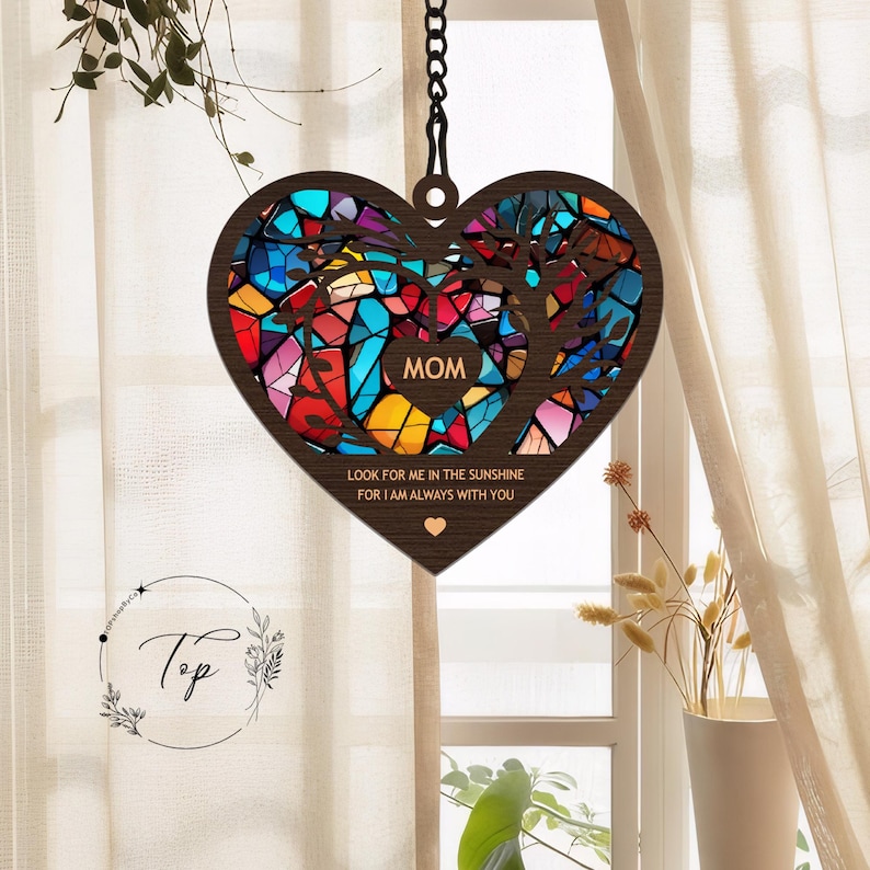 May include: A wooden heart-shaped wind chime with a stained glass design. The heart is decorated with colorful glass pieces and the words "MOM" and "Look for me in the sunshine for I am always with you".