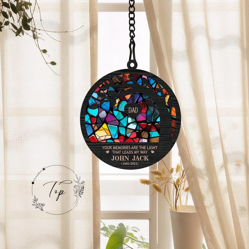 May include: A black wooden memorial wind chime with a stained glass tree design. The text reads "DAD, YOUR MEMORIES ARE THE LIGHT THAT LEADS MY WAY, JOHN JACK (1963-2024)"