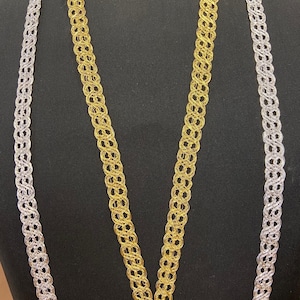 Puede incluir: Dos largos de adorno decorativo, uno plateado y otro dorado, se muestran en un maniquí negro. El adorno está hecho de un material tejido en forma de cadena.