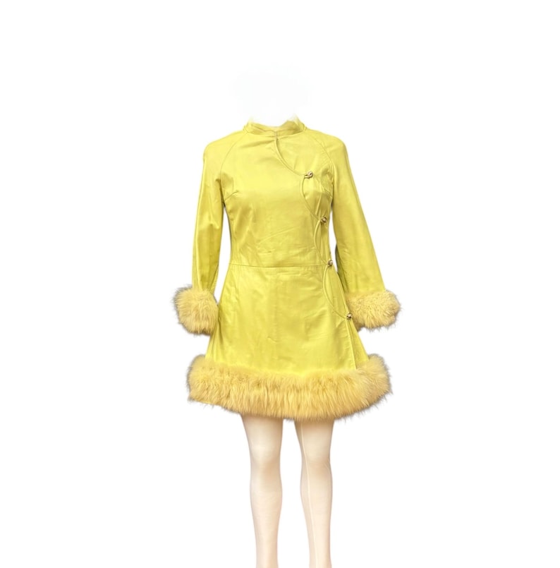 May include: A bright yellow dress with long sleeves and a mandarin collar. The dress features fur trim on the cuffs and hem. The dress has a wrap-style closure with decorative buttons.