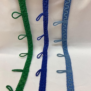 Könnte beinhalten: Drei verschiedene Farben von Besatz mit Quasten. Der Besatz ist grün, blau und hellblau. Der Besatz ist gewebt und hat ein dekoratives Muster.
