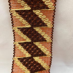 Può includere: Finitura tessuta marrone, arancione e beige con un motivo a chevron.