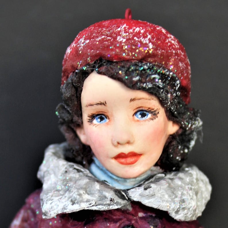 May include: A handmade doll with a red beret, a white fur collar, and a burgundy coat. The doll has blue eyes and a painted face.