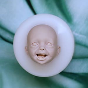 Peut inclure: Un moule en silicone blanc pour fabriquer une tête de poupée bébé. Le moule est en forme de tête de bébé avec une expression souriante.