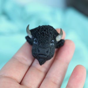Könnte beinhalten: Eine schwarze Bisonkopfskulptur aus Polymer Clay. Die Skulptur ist mit Fell detailliert und hat ein realistisches Aussehen.