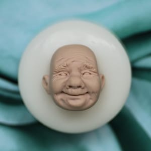 以下が含まれることがあります： 高齢者のリアルな顔の詳細な作りに適したシリコンモールド。モールドは白で、顔は薄い茶色です。