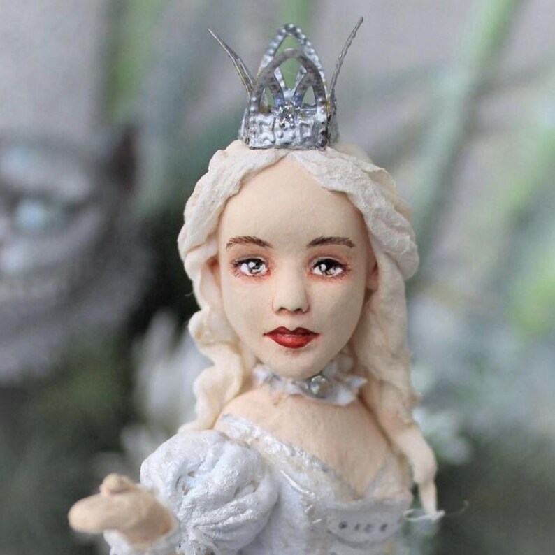 May include: A porcelain doll with a white dress and a silver crown. The doll has long blonde hair and blue eyes.