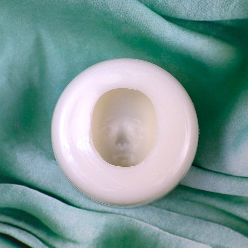 Pu&ograve; includere: Uno stampo in silicone bianco con un'impressione a forma di viso. Lo stampo &egrave; su uno sfondo di tessuto verde chiaro.