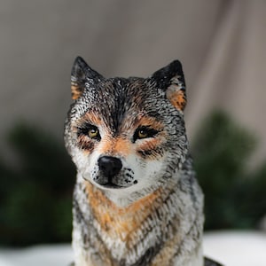 Könnte beinhalten: Handbemalte Wolfsfigur. Die Skulptur zeigt eine realistische Darstellung eines Wolfskopfes mit grauem, braunem und orangefarbenem Fell. Der Wolf hat gelbe Augen und eine schwarze Nase, die ein lebensechtes Aussehen einfangen.