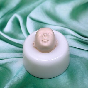 Pu&ograve; includere: Uno stampo in silicone bianco per realizzare una testa di bambola. Lo stampo &egrave; posto su una superficie di tessuto verde. Lo stampo &egrave; vuoto e pronto per essere utilizzato.