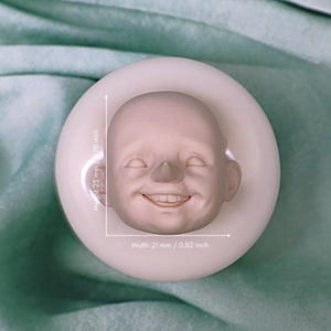 Puede incluir: Un molde de silicona blanco para hacer una pequeña cara sonriente. El molde mide 2,5 pulgadas de alto y 0,82 pulgadas de ancho.