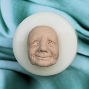 Könnte beinhalten: Eine detaillierte Silikonform eines lächelnden Gesichts einer älteren Person. Die Form ist weiß und das Gesicht ist hellbraun.