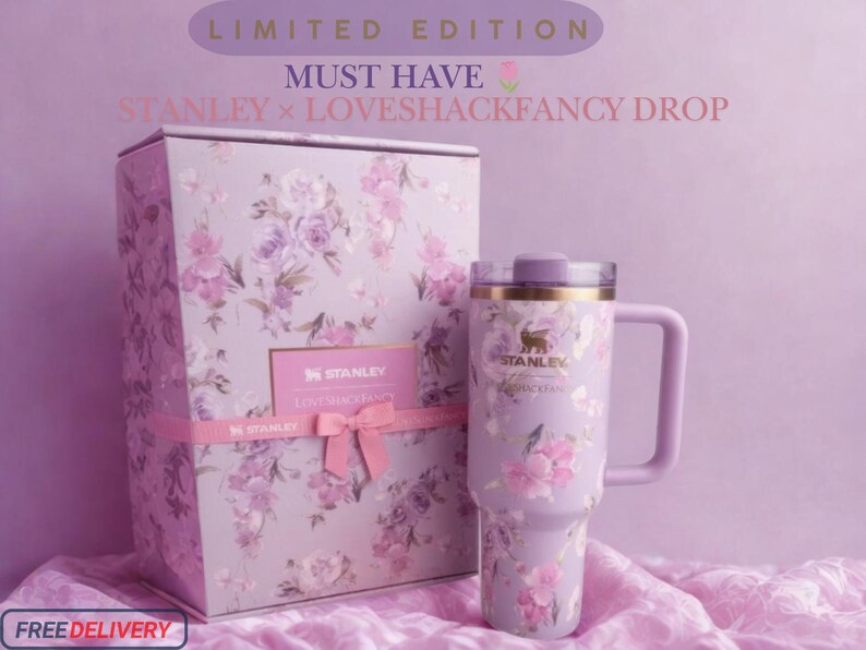Puede incluir: Un vaso Stanley de color lavanda con un estampado floral y una caja a juego con el texto LIMITED EDITION MUST HAVE STANLEY x LOVESHACKFANCY DROP. El vaso tiene un asa, una tapa y el logotipo de Stanley impreso en la parte frontal.