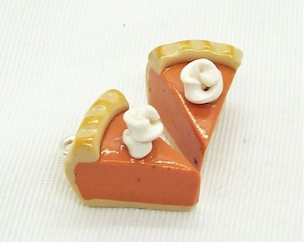 May include: Two miniature pumpkin pie slices with a dollop of white frosting on top. The pie crust is a light brown color and the filling is a vibrant orange.