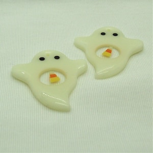 May include: Two white ghost-shaped ornaments with black eyes and a candy corn cutout in the center.