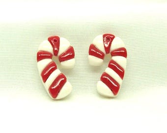 May include: Two candy cane-shaped earrings. Each earring features a white base with red stripes, mimicking the classic holiday treat. The earrings are small and curved, with a glossy finish, perfect for festive occasions.