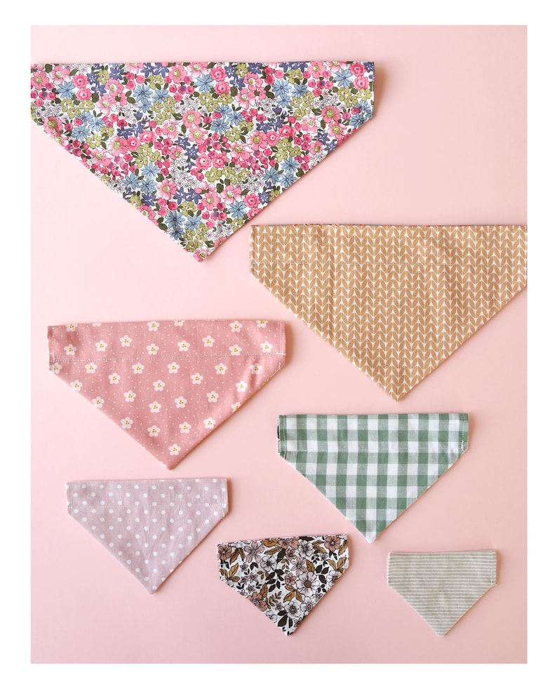 May include: A collection of seven triangular bandanas in various patterns and colors, including floral, polka dot, gingham, and striped designs. The bandanas are arranged on a light pink surface.