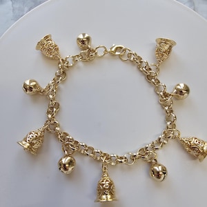 May include: A gold chain bracelet with multiple small bells hanging from it. The bells are intricately designed and have a shiny finish.