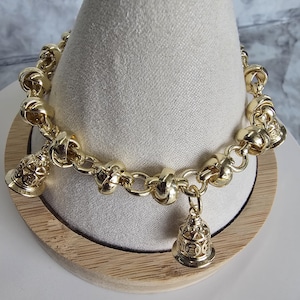 May include: A gold chain bracelet with three bell charms. The bracelet is made of thick, twisted links and the charms are detailed with intricate designs.