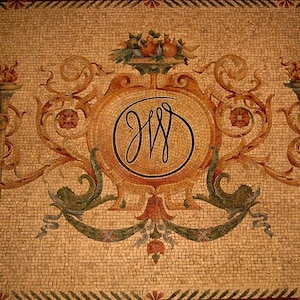 May include: A mosaic tile design featuring a central emblem with the intertwined letters "JW" within a circle. The emblem is surrounded by ornate scrollwork, floral elements, and two torch-like designs. The color palette includes shades of brown, gold, and green.