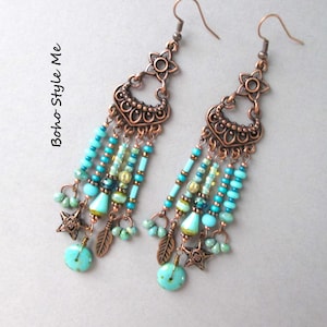 Puede incluir: Pendientes estilo boho con cuentas turquesas y azules, abalorios de estrella y pluma, y detalles metálicos color cobre. Los pendientes tienen un diseño floral en la parte superior y están diseñados para orejas perforadas.