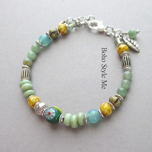 May include: A beaded bracelet featuring light green, yellow, and blue beads interspersed with silver-toned metal spacers and a leaf charm. The bracelet includes a lobster claw clasp and features the text Boho Style Me printed on the image.