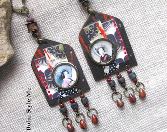 May include: A pair of dangle earrings featuring a house-shaped metal frame with a collage print of a person holding a parasol. The earrings include bronze-toned hardware, small dark beads, and three dangling charms with red and gray accents.