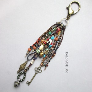 May include: A decorative keychain featuring a bronze-toned lobster clasp attached to multiple strands of assorted beads in shades of turquoise, red, brown, and black. The accessory includes a small metal key charm and the text Boho Style Me.