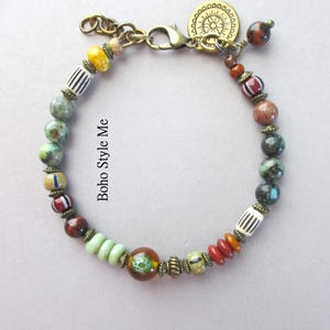 K&ouml;nnte beinhalten: Ein mehrfarbiges Perlenarmband mit einer Vielzahl von runden, zylindrischen und scheibenf&ouml;rmigen Perlen in Gr&uuml;n-, Braun-, Rot-, Gelb- sowie Schwarz-Wei&szlig;-gestreiften T&ouml;nen. Das Armband enth&auml;lt antikfarbene Messing-Abstandshalter und einen Karabinerverschluss.