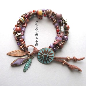 May include: A multi-strand bracelet with a bohemian style. The bracelet features a variety of beads in shades of purple, brown, and red. It includes a turquoise and copper-colored circular charm, feather charms, and the text "Boho Style Me".
