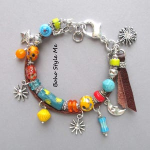 Puede incluir: Una pulsera de cuentas coloridas con varios dijes. Presenta una mezcla de cuentas redondas y cilíndricas en azul, amarillo, naranja y rojo. Los dijes incluyen estrellas, una luna y soles. El texto "Boho Style Me" es visible.