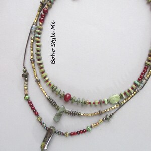 Puede incluir: Un collar de cuentas de varias hebras con cuentas verdes, rojas y doradas met&aacute;licas y dos colgantes de piedra. El collar incluye peque&ntilde;as cuentas cil&iacute;ndricas y redondas, con el texto Boho Style Me impreso verticalmente en el centro.