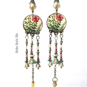 May include: A pair of long dangle earrings featuring circular discs with a red floral print. Each earring has three hanging strands composed of green, pink, and clear beads, bronze-toned metal accents, and small bell-shaped charms. The text Boho Style Me is visible.