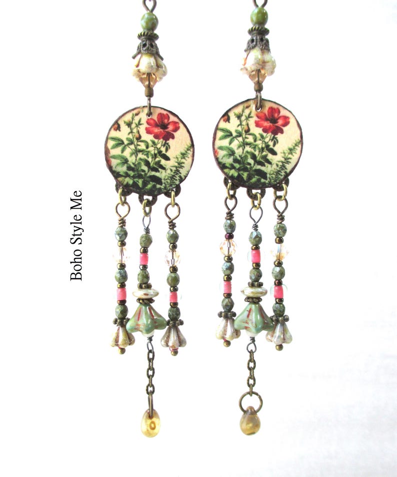 May include: A pair of long dangle earrings featuring circular discs with a red floral print. Each earring has three hanging strands composed of green, pink, and clear beads, bronze-toned metal accents, and small bell-shaped charms. The text Boho Style Me is visible.