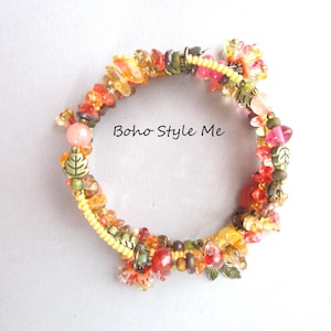 May include: A multi-strand wrap bracelet featuring an assortment of yellow, orange, and red beads, interspersed with small bronze-toned metal leaf charms. The text "Boho Style Me" is printed in the center of the circular arrangement of beads.
