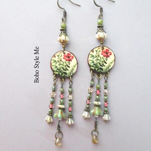 May include: A pair of dangle earrings featuring bronze-toned hooks, green and cream floral-patterned circular discs, and multi-strand drops with green, pink, and clear beads, small bell-shaped charms, and teardrop accents. The text Boho Style Me is visible.